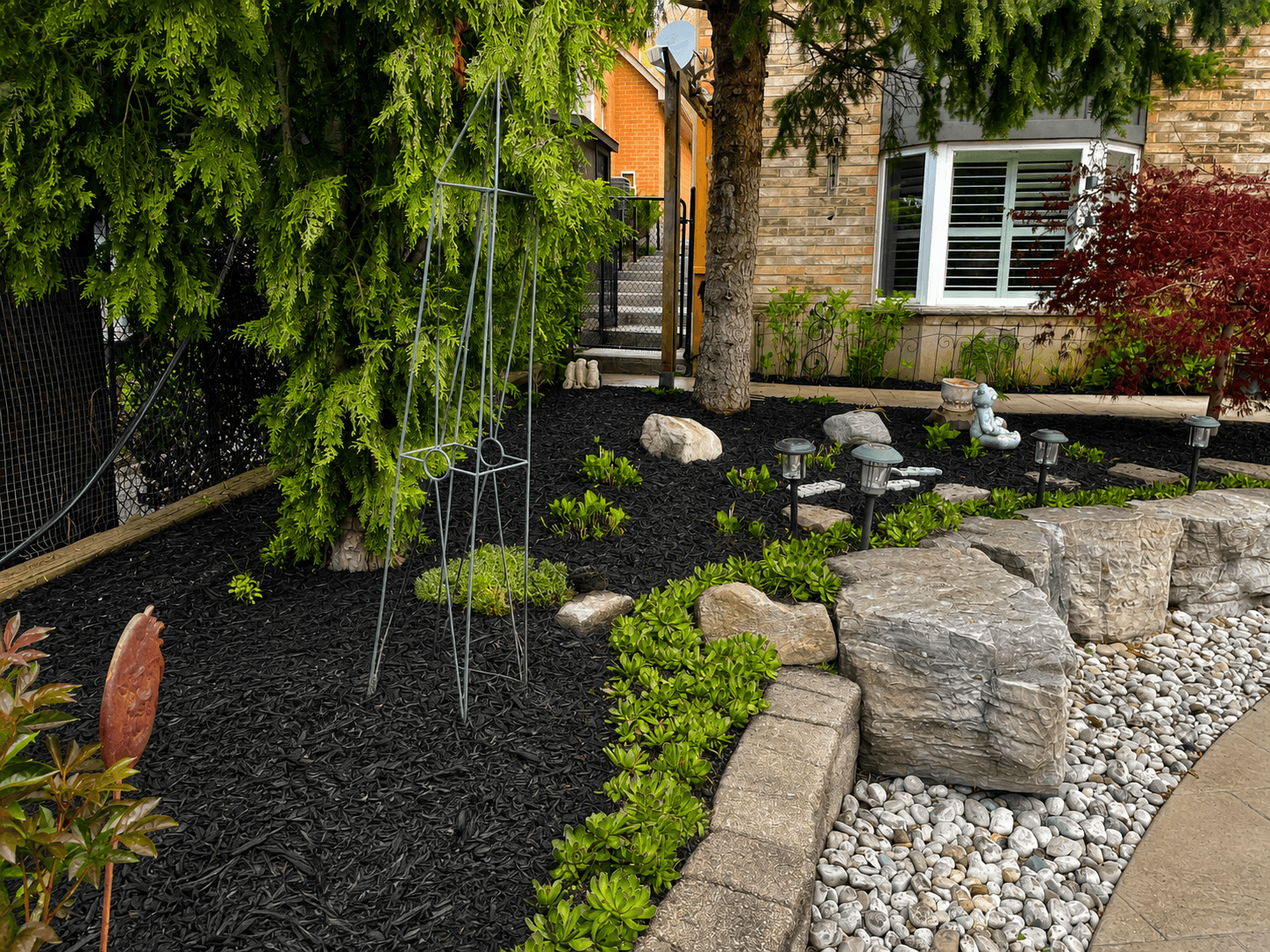 Front yard landscape with black mulch beds, armour boulders, and river rock border