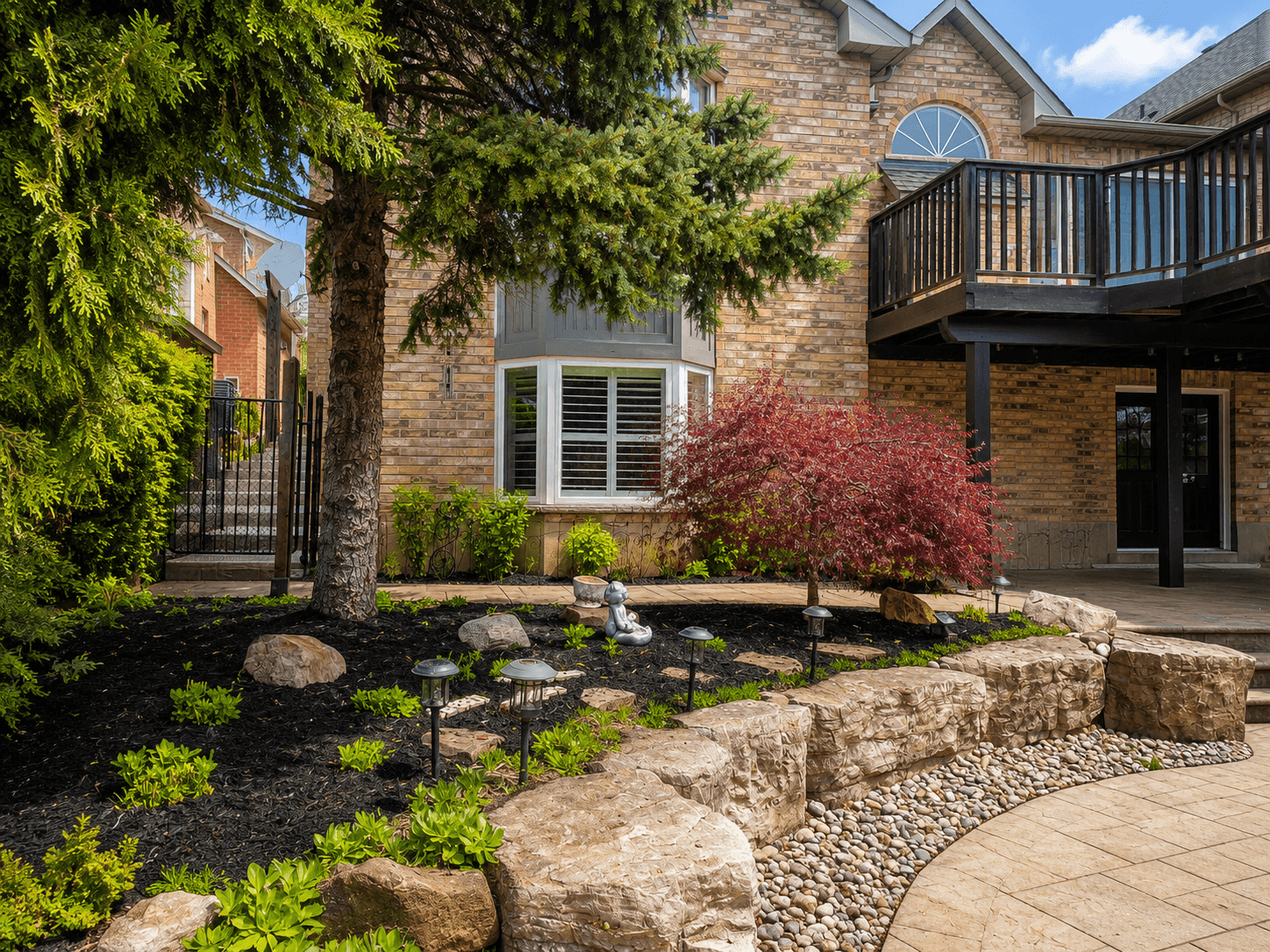 Armour stone landscape feature with river rock, lighting, and Japanese maple